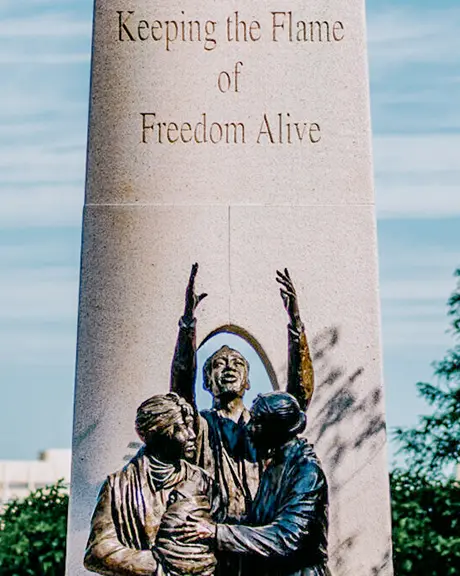 The Tower of Freedom monument in Windsor with sculpted figures and a city skyline in the background.
